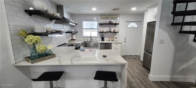 kitchen featuring light stone counters, white cabinets, wall chimney exhaust hood, a breakfast bar, and hardwood / wood-style floors