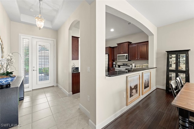 kitchen with stainless steel appliances, pendant lighting, a raised ceiling, and light wood-type flooring