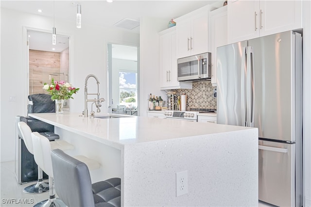 kitchen with decorative light fixtures, stainless steel appliances, a breakfast bar, and white cabinetry