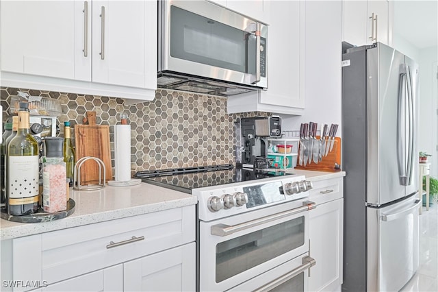 kitchen featuring stainless steel appliances, white cabinets, light stone counters, and decorative backsplash