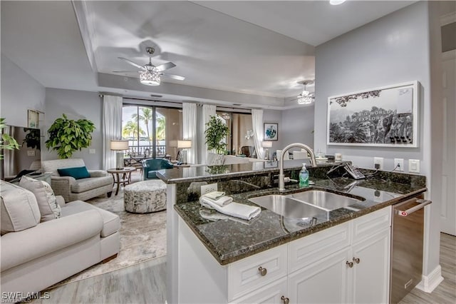 kitchen with a kitchen island with sink, light wood-type flooring, dark stone countertops, sink, and white cabinets