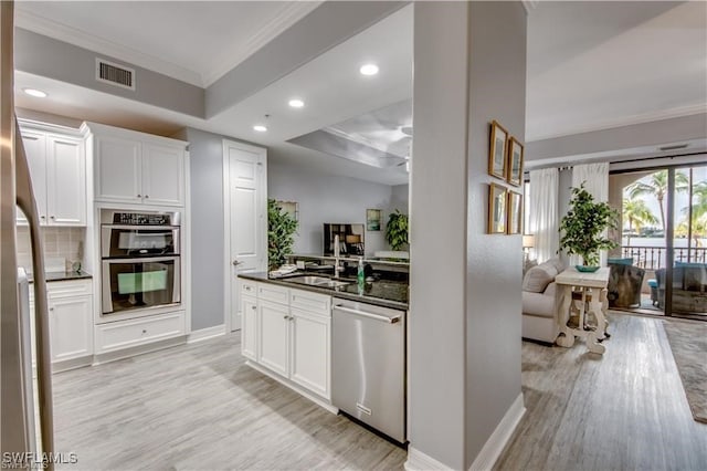 kitchen with decorative backsplash, stainless steel appliances, white cabinets, sink, and light hardwood / wood-style flooring