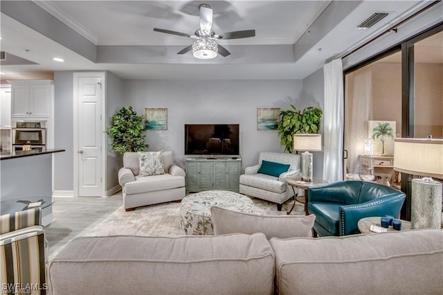 living room with light hardwood / wood-style floors, ornamental molding, a raised ceiling, and ceiling fan