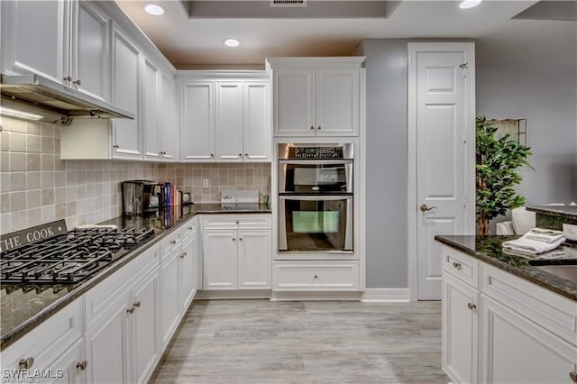 kitchen featuring white cabinets, tasteful backsplash, dark stone counters, appliances with stainless steel finishes, and light wood-type flooring