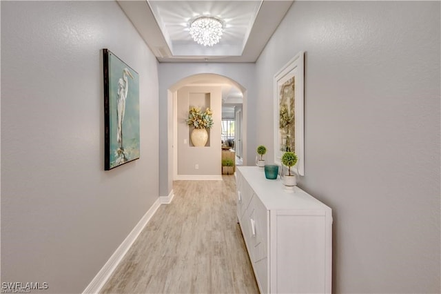 hallway with an inviting chandelier, light hardwood / wood-style flooring, and a raised ceiling