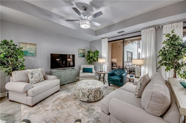 living room featuring light wood-type flooring, ceiling fan, and a raised ceiling