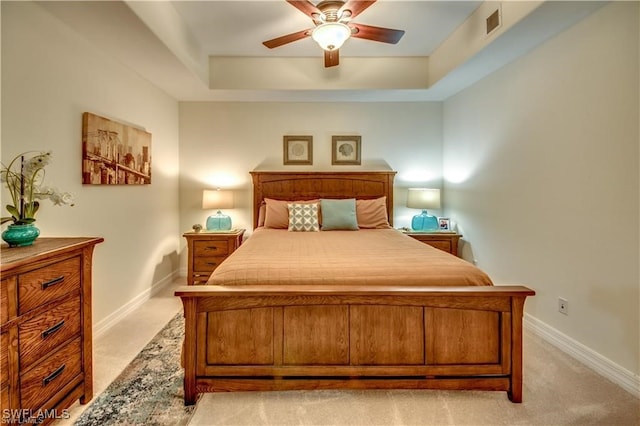 carpeted bedroom with a raised ceiling and ceiling fan