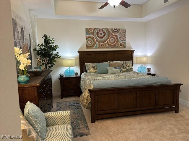 bedroom with ceiling fan, light colored carpet, and a raised ceiling