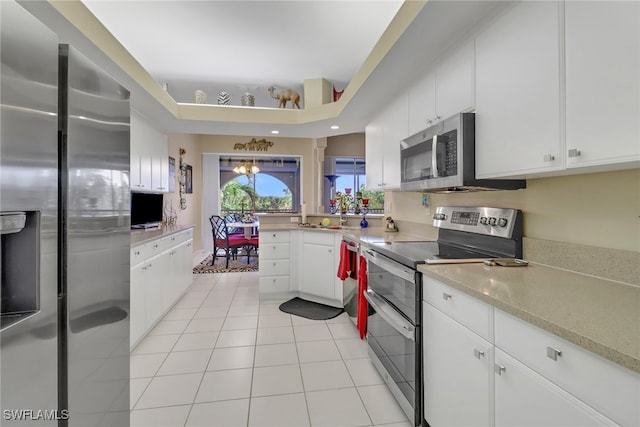 kitchen with a tray ceiling, a notable chandelier, white cabinets, appliances with stainless steel finishes, and light tile patterned floors