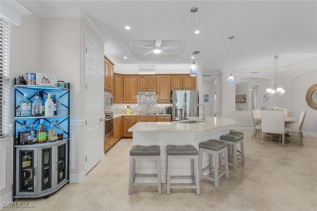 kitchen with an island with sink, stainless steel appliances, sink, ceiling fan with notable chandelier, and decorative light fixtures