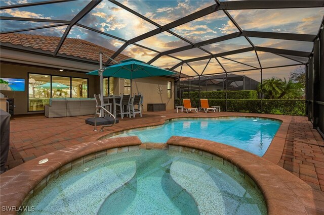 pool at dusk featuring an in ground hot tub, a patio, and glass enclosure