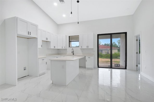 kitchen featuring a high ceiling, a kitchen island, hanging light fixtures, and white cabinets