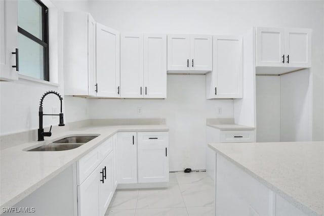 kitchen with light stone counters, white cabinetry, and sink