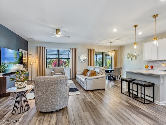 living room with ceiling fan with notable chandelier, light wood-type flooring, and a wealth of natural light