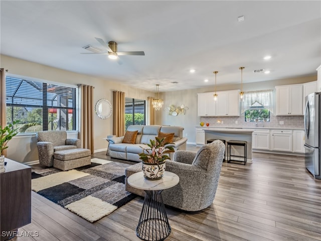 living room with ceiling fan with notable chandelier, hardwood / wood-style floors, and a wealth of natural light