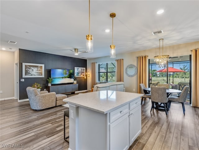 kitchen featuring light hardwood / wood-style floors, light stone countertops, hanging light fixtures, white cabinets, and a center island