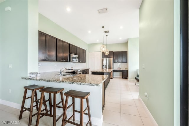 kitchen with kitchen peninsula, light stone countertops, decorative light fixtures, appliances with stainless steel finishes, and tasteful backsplash