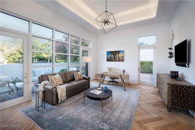 living room with a notable chandelier, plenty of natural light, a tray ceiling, and light parquet floors