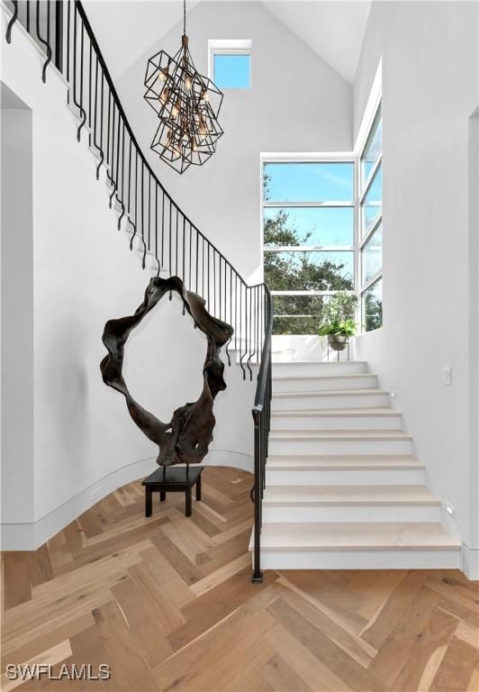 stairway featuring a notable chandelier, parquet floors, and high vaulted ceiling