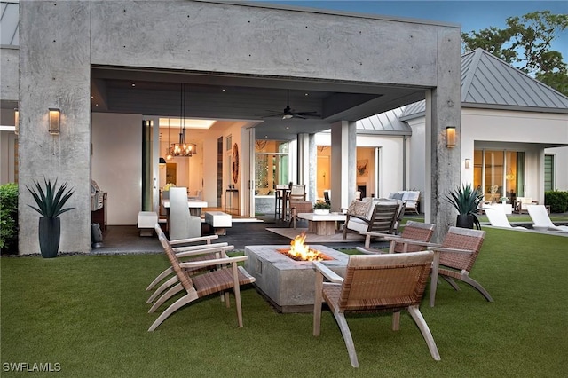 rear view of property with a lawn, ceiling fan, and an outdoor living space with a fire pit