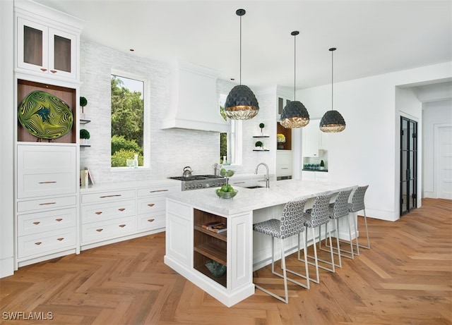 kitchen featuring white cabinetry, a center island with sink, sink, and custom exhaust hood