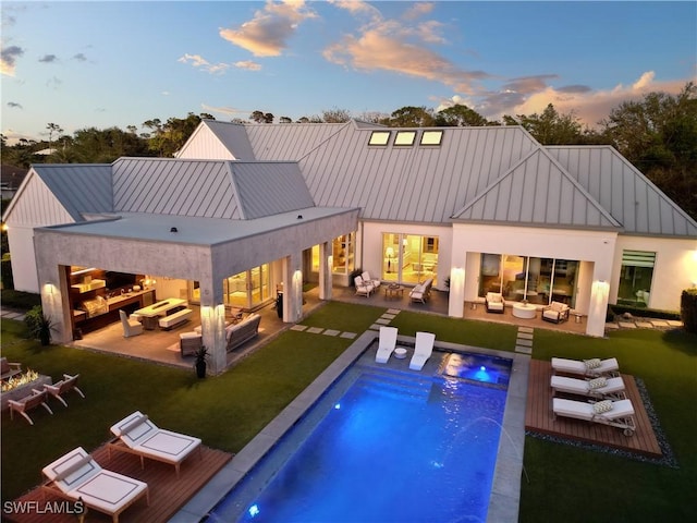 back house at dusk with an outdoor living space with a fireplace, a patio area, and pool water feature