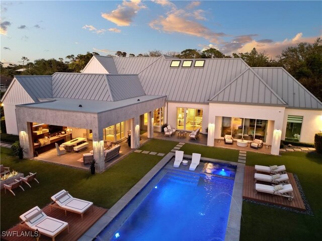 581 Myrtle Rd, Naples, FL 34108 - back of house at dusk featuring an outdoor living space with a fire pit, a standing seam roof, an outdoor pool, and stucco siding