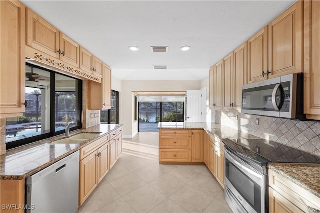 kitchen with stone counters, sink, stainless steel appliances, backsplash, and kitchen peninsula