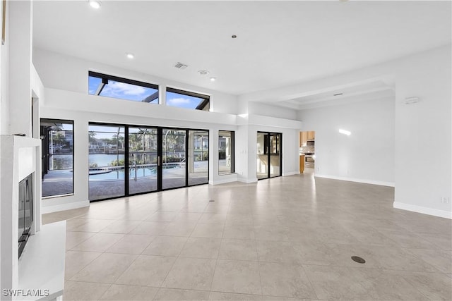 unfurnished living room with a high ceiling, a water view, and light tile patterned floors