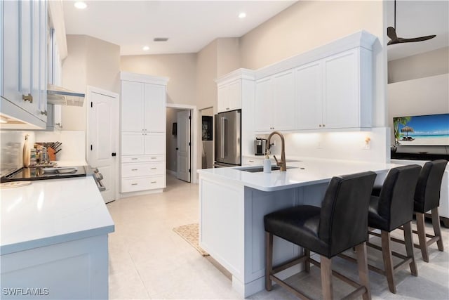 kitchen featuring a kitchen bar, kitchen peninsula, stainless steel refrigerator, white cabinets, and sink