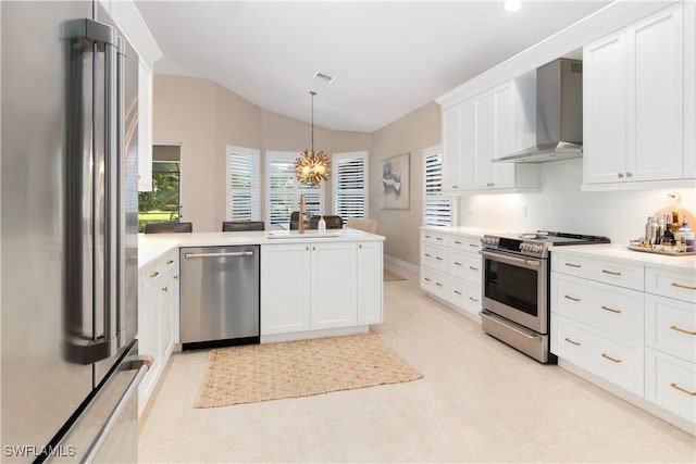 kitchen featuring pendant lighting, appliances with stainless steel finishes, white cabinetry, wall chimney range hood, and an inviting chandelier