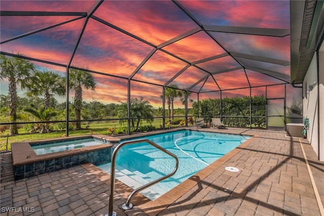 pool at dusk with an in ground hot tub, a patio area, and a lanai