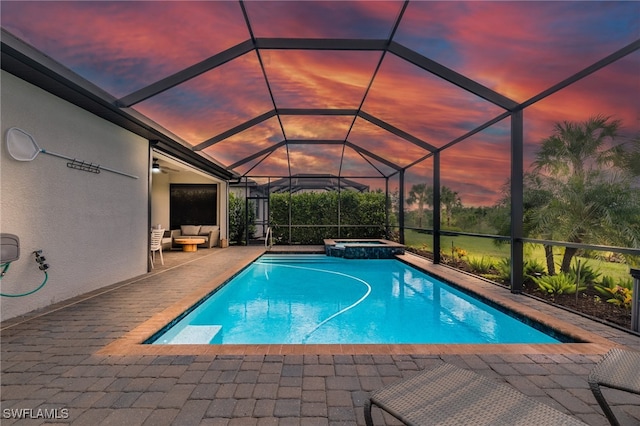 pool at dusk featuring an in ground hot tub, glass enclosure, and a patio area