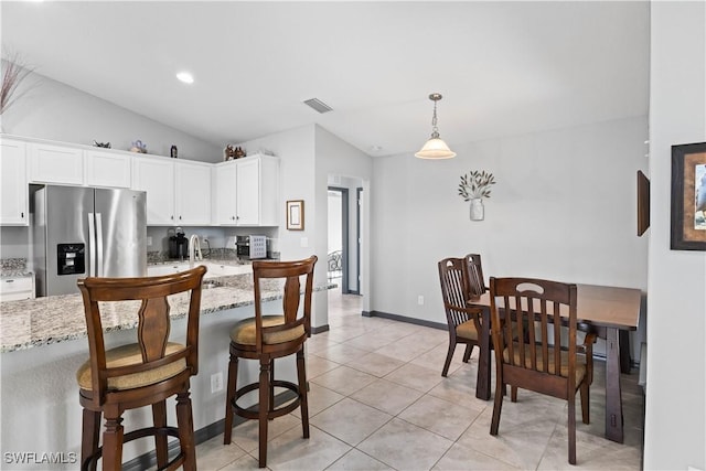 kitchen featuring lofted ceiling, hanging light fixtures, light stone countertops, white cabinets, and stainless steel fridge