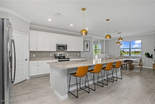 kitchen with an island with sink, light stone countertops, pendant lighting, white cabinetry, and appliances with stainless steel finishes