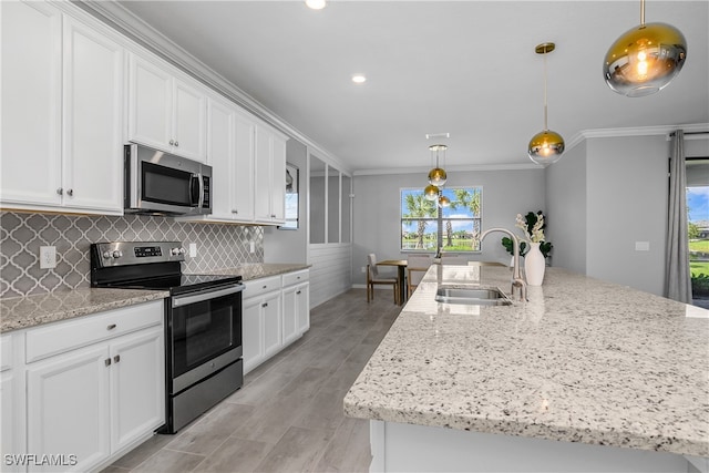 kitchen with pendant lighting, stainless steel appliances, a kitchen island with sink, a sink, and white cabinets