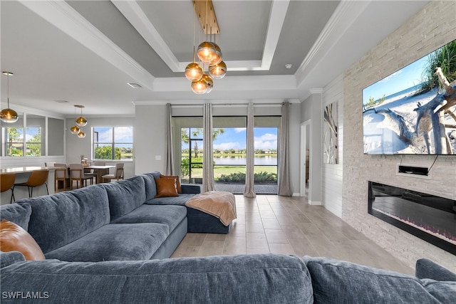 living room with light wood-type flooring, a stone fireplace, crown molding, a tray ceiling, and a chandelier