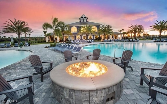 pool at dusk with a patio area, an outdoor fire pit, and a community pool