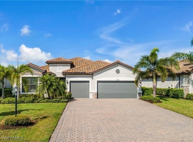 mediterranean / spanish home featuring a garage, stone siding, a tiled roof, decorative driveway, and a front lawn