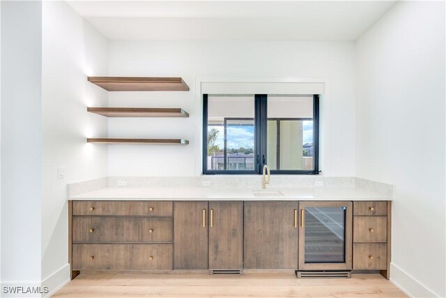 bar with beverage cooler, light hardwood / wood-style floors, and sink