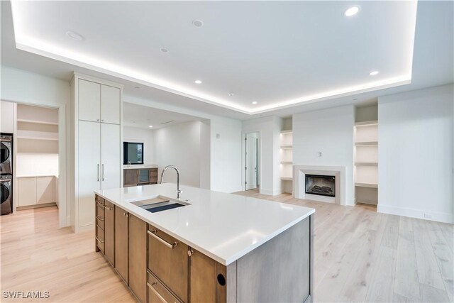 kitchen with stacked washing maching and dryer, a raised ceiling, sink, and a center island with sink