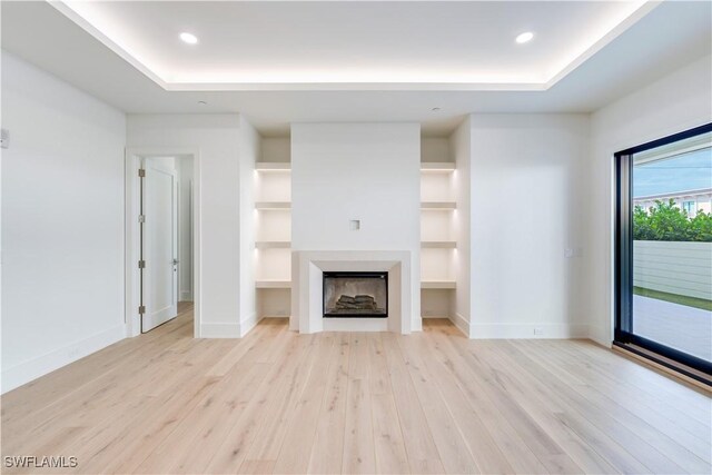 unfurnished living room with built in shelves, light hardwood / wood-style flooring, and a tray ceiling