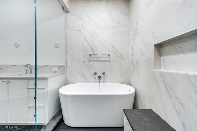 bathroom with vanity, tile walls, and a bath