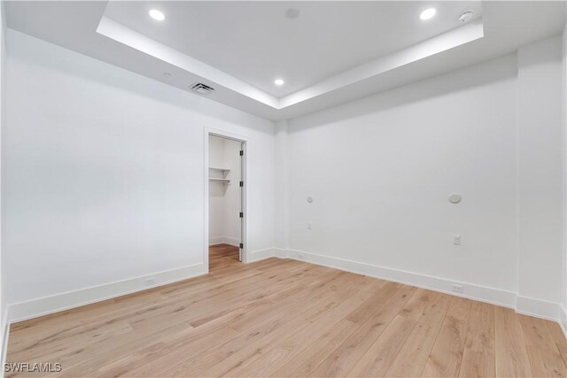 spare room featuring a tray ceiling and light hardwood / wood-style flooring