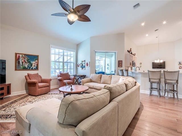 living room featuring lofted ceiling, ceiling fan with notable chandelier, and light wood-type flooring