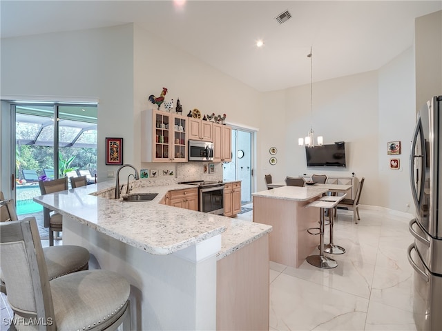 kitchen with kitchen peninsula, hanging light fixtures, a breakfast bar, sink, and stainless steel appliances