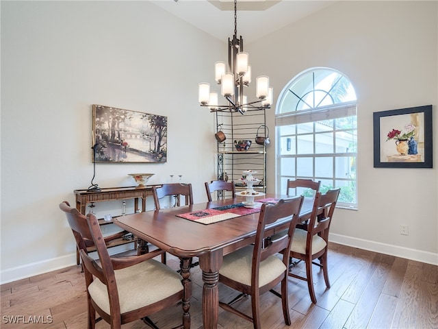 dining room featuring a notable chandelier, wood-type flooring, and a high ceiling