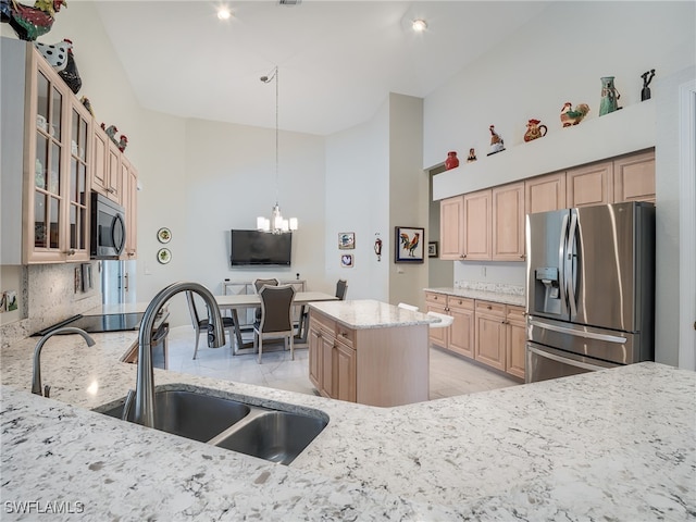 kitchen featuring sink, a kitchen island, stainless steel appliances, light stone counters, and an inviting chandelier