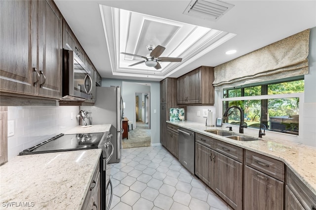 kitchen featuring ceiling fan, a raised ceiling, light stone countertops, sink, and stainless steel appliances