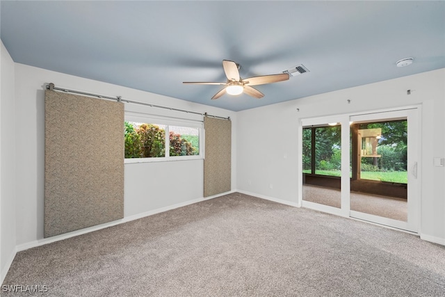 spare room featuring carpet, a barn door, and ceiling fan